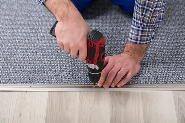 Worker securing carpet along the edge of a floor | Carpetland USA Granite & Flooring