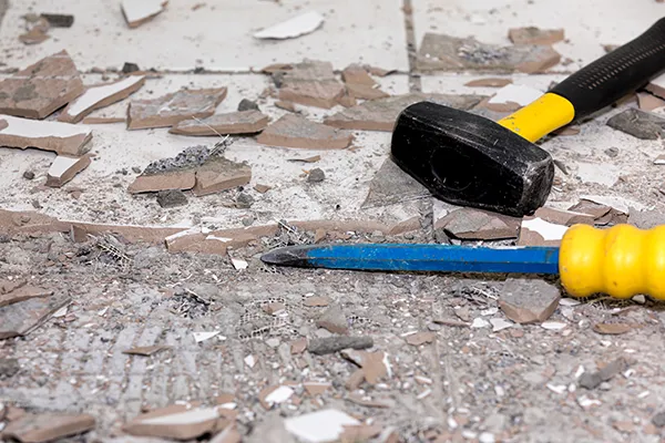 Removing damaged floor tiles with a pry bar and mallet | Carpetland USA Granite & Flooring