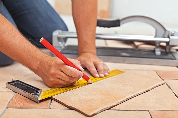 Worker measuring a tile before making a floor repair | Carpetland USA Granite & Flooring