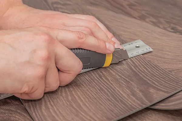 Worker cutting vinyl flooring with a utility knife | Carpetland USA Granite & Flooring